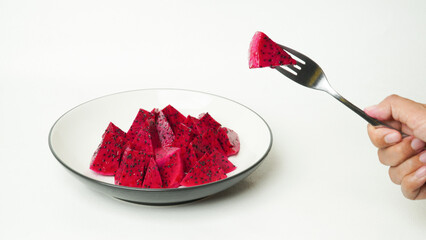 Red dragon fruit that has been cut into small pieces and served on a white plate and placed in a white place (isolated white).