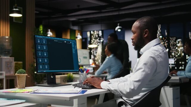 African american male checking web AI chatbot responses for some tasks, working after hours to meet business objectives. Problem solving with futuristic tech and machine learning. Camera A.