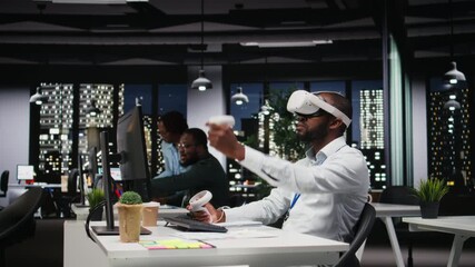 Young black businessman using virtual reality headset and other devices to build a strategy, forecasting projections and documenting risk assessment for success. Business goals. Camera A. - Powered by Adobe