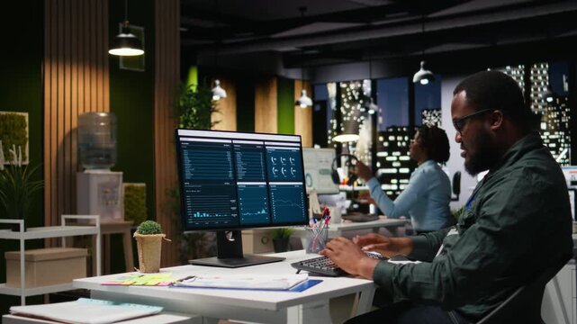 Office worker reviewing KPI metrics on monitor and analytics on desktop, building a vision and business strategy to accomplish objectives and success. Professional mindset after hours. Camera A.