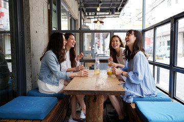 Four women laughing and chatting over drinks at a bright cafe table, warm daytime indoor scene. Generative AI