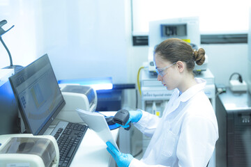 A diligent female scientist in a high-tech lab cross-references a printed report with data graphs on her computer, meticulously verifying experimental results for a research study.