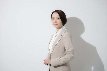  ベージュのスーツを着た営業など、美人な女性のビジネス上半身　立つのカメラ目線　白背景真剣な表情
