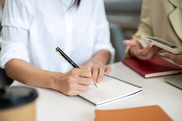 Close up of a woman student's hands holding pen writing in notebook aside teacher on table.