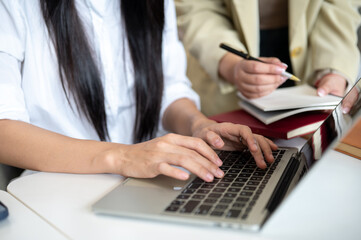Obraz premium Close up of a woman student's hands on laptop with teacher holding pen checking her work at table.