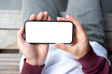 A man's hands holding white screen smartphone in horizontal while sitting outdoor on wooden bench.