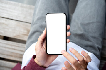 A man's hands holding blank screen smartphone with fingers hovering sitting outdoor on wooden bench.