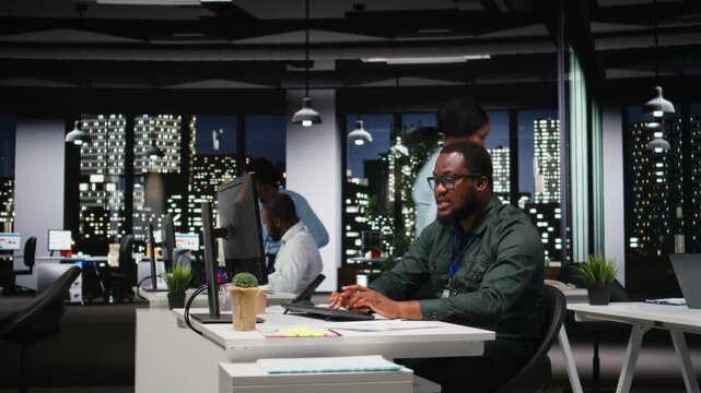 African american advisor focusing on a complex problem in a dark office at night, strategizing and envisioning options on desktop. Seeking a logical solution through careful deduction. Camera A.