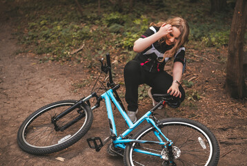 woman in stylish sportswear sits beside bicycle on a forest trail, smiling and enjoying beautiful...