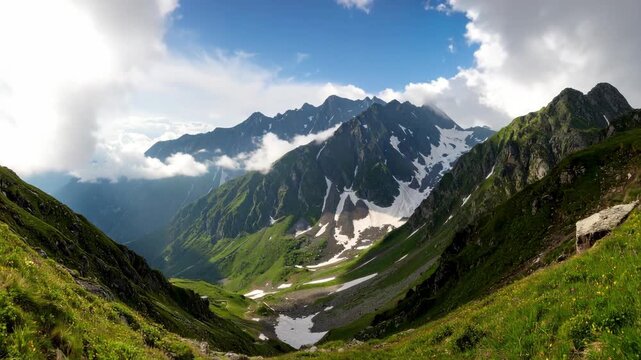 Panoramic vista of green mountains with snow patches under a partly cloudy sky during the day, offering scenic tranquility and natural beauty