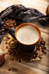 Flat white coffee in a black cup with coffee beans on rustic wooden table.