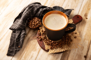Flat white coffee in a black cup with coffee beans on rustic wooden table.
