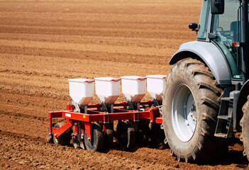 a modern tractor equipped with a seed planting machine operating in a freshly plowed field. 