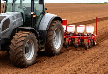 a modern tractor equipped with a seed planting machine operating in a freshly plowed field. 