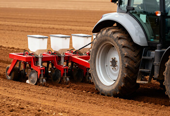 a modern tractor equipped with a seed planting machine operating in a freshly plowed field. 