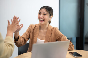 Asian businesswoman clapping hands high five coworker during office meeting aside laptop on table