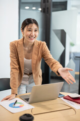 Asian businesswoman office worker extending a hand welcoming handshaking over laptop on wooden table