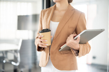 Close up businesswoman office worker holding coffee and laptop while standing or walking in building
