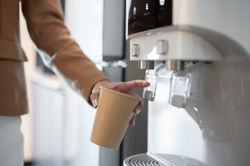 Close up businesswoman or office worker's hand holding paper cup getting hot water or making coffee.