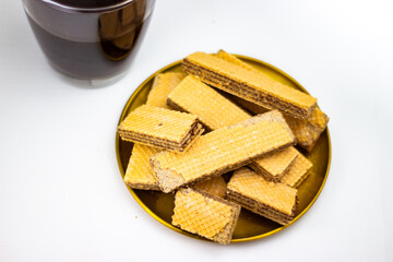 Golden plate piled with rectangular chocolate wafer cookies next to a dark beverage