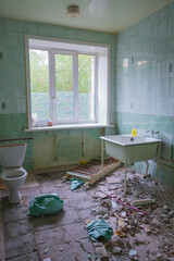 bathroom shows signs neglect and decay, with missing tiles, an exposed floor, and visible debris around toilet and bathtub. natural light enters through window. close up.