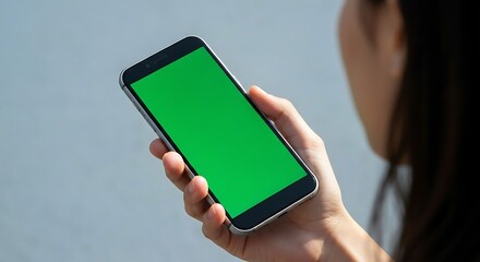 Over the shoulder view of a person holding a modern smartphone with a blank green screen display.