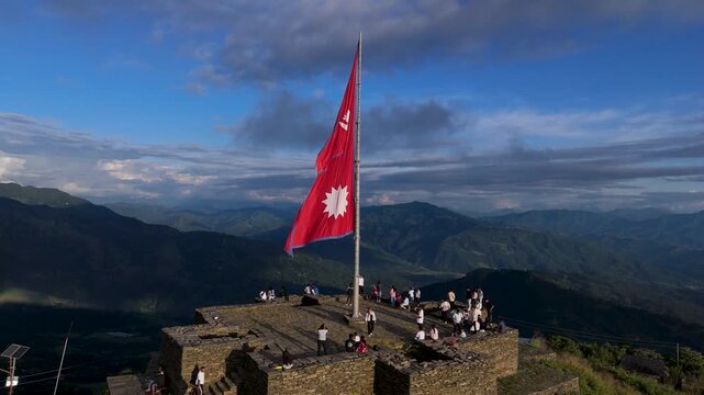 Cinematic aerial drone shot of large Nepal national flag waving on high mountain top, crimson red double triangle flag with sun and moon emblems, patriotism and pride concept