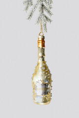 Minimal creative aesthetic view of Champagne bottle Christmas ornament hanging on fir tree branch. New Year golden toy as sparkling wine. Festive Winter holiday still life. Concept of celebration.
