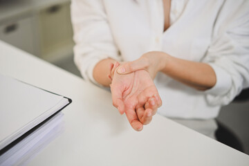 Obraz na płótnie Canvas Businesswoman suffering from hand fatigue, rubbing wrist to relieve pain caused by overuse or office work