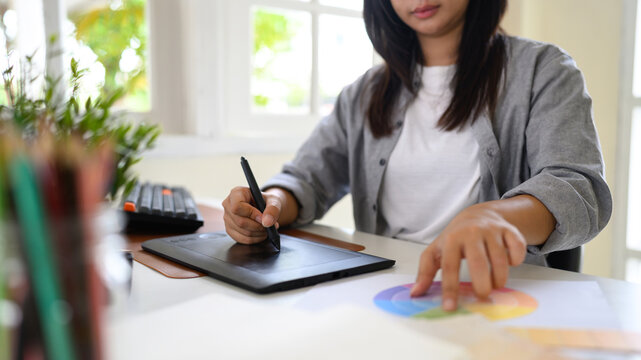 Close up of a graphic designer working with a drawing tablet and color wheel while developing creative design concepts - Powered by Adobe