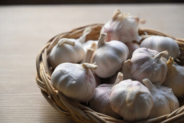 Close up of fresh garlic bulbs placed in a woven basket, natural light highlighting texture and freshness