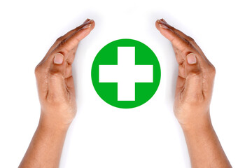 Hands protecting a green medical cross symbol on white background.