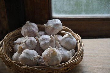 Close up of fresh garlic bulbs arranged in a wicker basket by a window with natural light