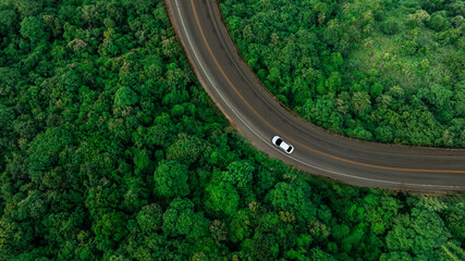 Aerial view of dark green forest road and white electric car Natural landscape and elevated roads Adventure travel and transportation and environmental protection concept	
