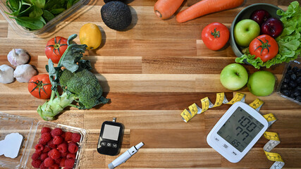 Flat lay of fresh fruits and vegetables with glucose meter, blood pressure monitor, and measuring tape on wooden table