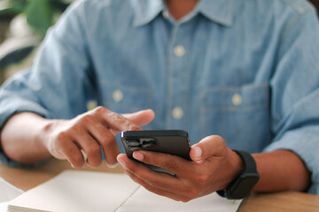 Close up of man using smartphone with notebook on desk. Modern lifestyle, digital technology, online communication, social media, and business planning concept.