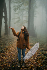 Woman feeling rain drops in a foggy autumn forest
