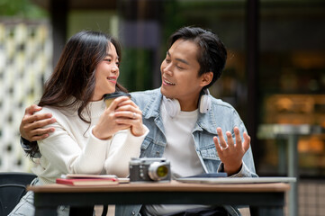 Young asian couple a man talking to woman holding coffee sitting at outdoor table in front of a cafe