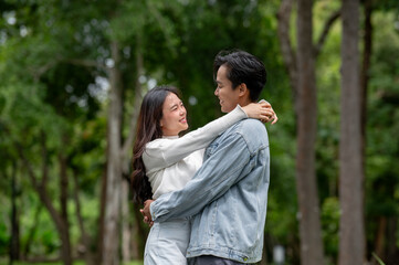 Fototapeta premium Young asian couple of man and woman holding and hugging each other while standing outdoors in park.
