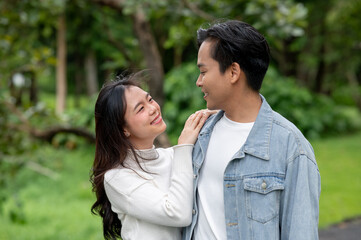Obraz premium Young asian couple locking eyes as woman holding man's shoulder standing or walking outdoors in park