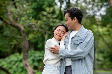 Fototapeta premium Young asian couple woman holding and resting head on man's shoulder while standing outdoors in park.