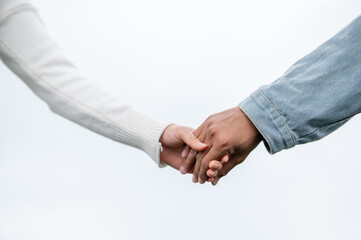 Close up of a young couple holding hands standing outdoors under bright sky or white background.