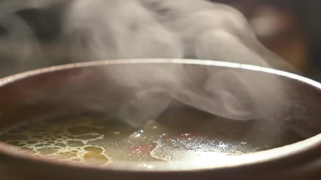 Steaming broth simmers in a metal pot, creating a comforting and warm atmosphere in a dimly lit restaurant, perfect for a chilly evening.