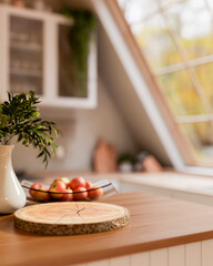 Tree stump chopping board with apples in glass plate on wooden cooking counter in roof window kitchen.