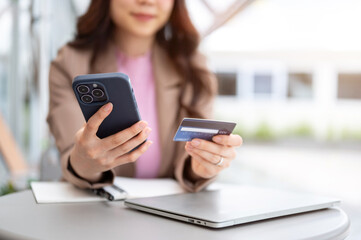 Asian business woman office worker holding phone and credit card sitting with laptop at cafe table