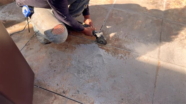 Trabajador De La Construcción Con Esmeril En Mano Trabajando en una obra cortando el piso para renovar o construir alba&ntilde;il en un dia de trabajo pesado 