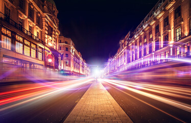 A vibrant, blurred London street scene showcases multicolored light trails amidst indistinct buildings, suggesting a nighttime urban environment with a lively, energetic mood.