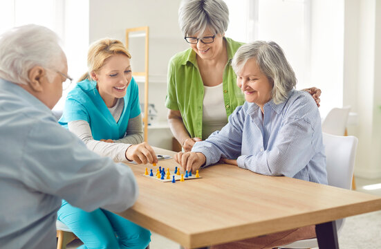 Supportive home care nurse and demente seniors having fun playing board game to preserve brain logical and analysis ability, mental agility and fine motor skills. Therapy in retirement home.