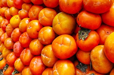 selective image of fresh ripe persimmon fruit (Diospyros kaki) displayed together at a local market for sale. ideal for fruit background and vegetarian diet or natural food design theme