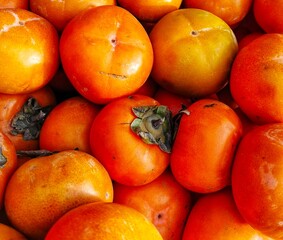 selective image of fresh ripe persimmon fruit (Diospyros kaki) displayed together at a local market for sale. ideal for fruit background and vegetarian diet or natural food design theme